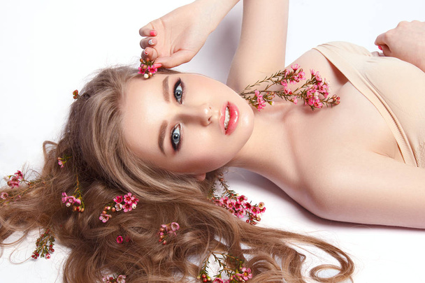 Portrait of young model with field flowers in wavy hair on white background - Photo, image