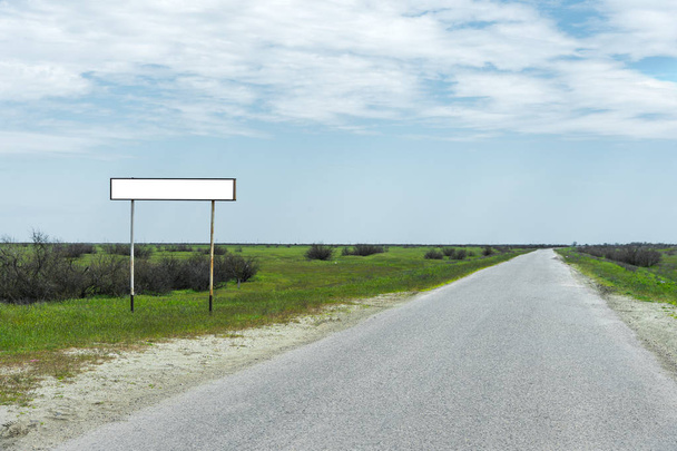 Lege oude verkeersbord voor de naam van een stad of dorp bevolkte gebied in de buurt van de weg op het platteland tegen een blauwe hemel en witte wolken omgeven door groen gras - Foto, afbeelding