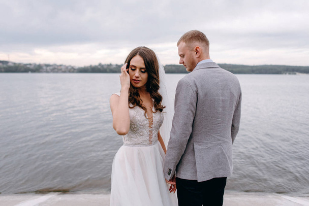 Detailní záběr na krásné novomanželé, drželi se za ruce a lodě na řece pozadí - Fotografie, Obrázek