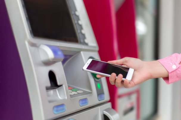 Nő, aki egy smartphone pénzügyi tranzakciók online a háttérben, ATM kabinet. Online NFC Banking koncepció - Fotó, kép