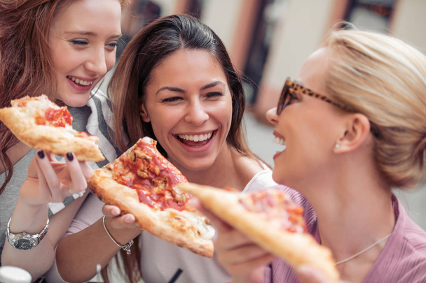Портрет трех молодых женщин, которые едят пиццу на открытом воздухе
 - Фото, изображение