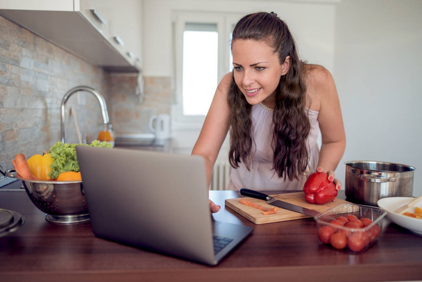 Mulher gostando de cozinhar e procurando receita no laptop
  - Foto, Imagem