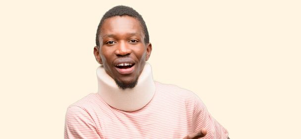 Afrikaanse zwarte man dragen van nek brace houdt iets in lege hand gewond - Foto, afbeelding