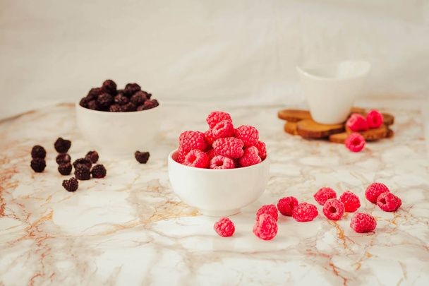 Raw raspberries and wild black, blackberries in white cups. Ligh - 写真・画像