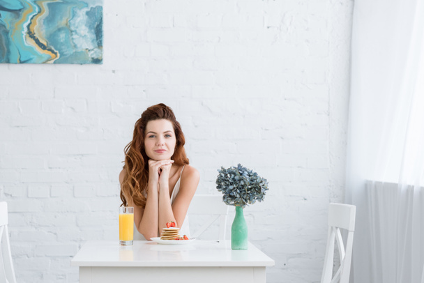 beautiful young woman with orange juice and pancakes with strawberry for breakfast at home looking at camera - Foto, afbeelding