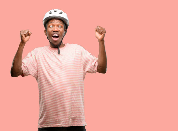 Musta mies yllään pyöräilykypärä onnellinen ja innoissaan juhlii voittoa ilmaista suurta menestystä, voimaa, energiaa ja positiivisia tunteita. Juhlii uutta työtä iloinen
 - Valokuva, kuva