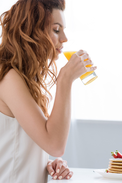 side view of beautiful young woman drinking orange juice at home - Fotografie, Obrázek