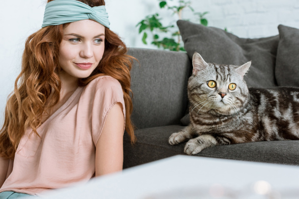 schöne junge Frau sitzt neben entzückender gestromter Katze zu Hause - Foto, Bild