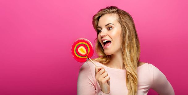 Beautiful young woman with big lollipop on pink background, copy space - Valokuva, kuva
