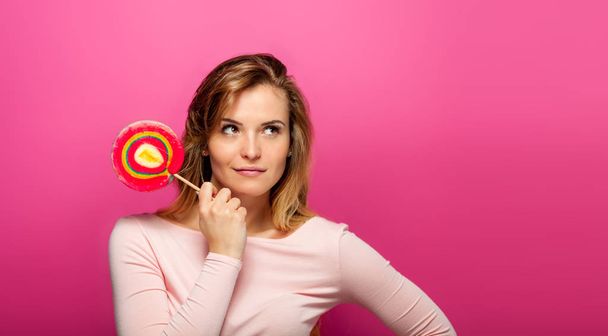 Beautiful young woman with big lollipop on pink background, copy space - Фото, зображення