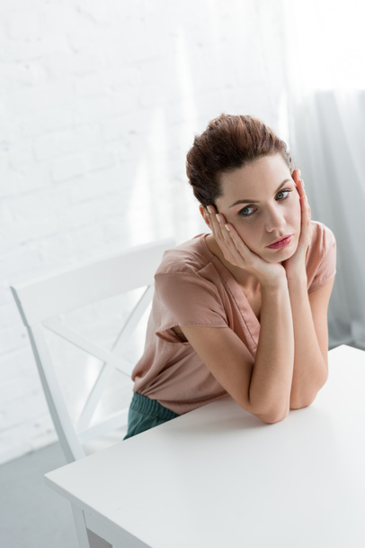 jeune femme déprimée assise à table devant un mur de briques blanches
 - Photo, image