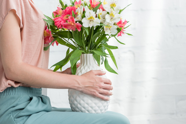 cropped shot of woman with flowers in vase in front of white brick wall - Photo, Image