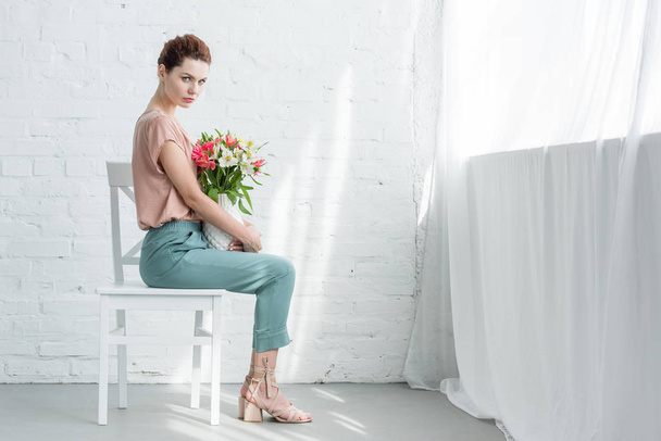 sensual young woman with flowers in vase in front of white brick wall - Foto, imagen