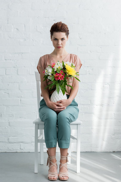 schöne junge Frau mit Blumen in Vase vor weißer Ziegelwand - Foto, Bild