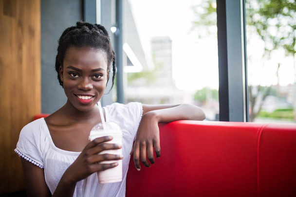 Jonge afro-Amerikaanse vrouw drankje milkshake in café - Foto, afbeelding
