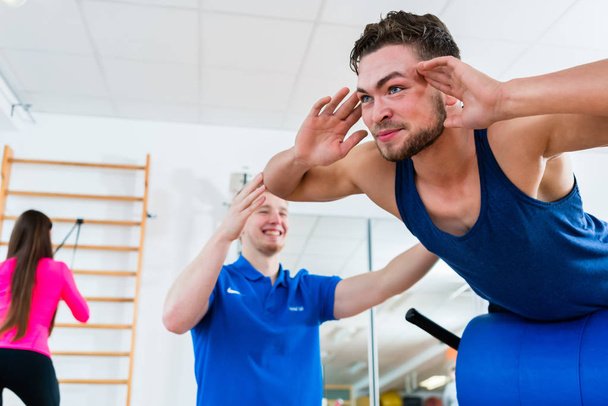 man at gym on workout bench getting assistance by personal trainer - Photo, Image