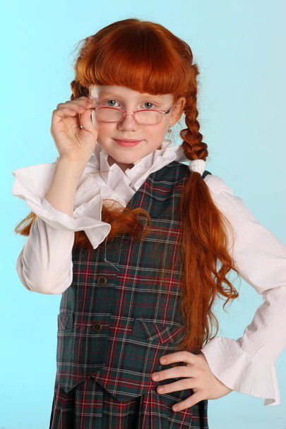 Portrait of beautiful little redhead girl is standing in a school uniform. Pretty attractive child poses with glasses artistically. The young schoolgirl is 8 years old. - Fotografie, Obrázek