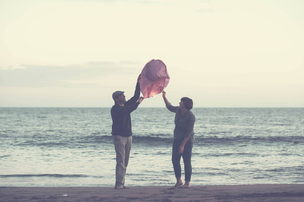 couple together forever dream and wish some desires, red Chinese lantern fly on the sky at the evening with ocean in the background. beach leisure activity in vacation, love concept - Photo, Image