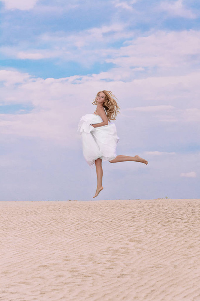 Woman in a wedding dress jumping up in the desert - Фото, зображення