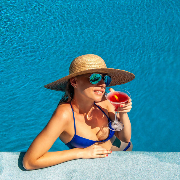 mujer con sombrero relajante en la piscina con un cóctel cosmopolitan - Fotoğraf, Görsel