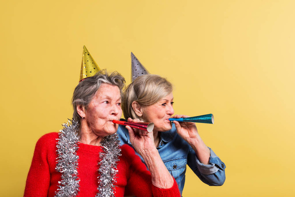 Portrait of a senior women in studio on a yellow background. Party concept. - Фото, изображение