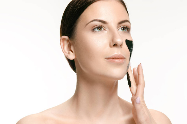 Giovane bella donna che applica una maschera per il viso del fango nero terapeutico. Trattamento termale
 - Foto, immagini