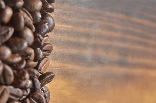 Many coffee beans lie on the left on a wooden background. - Foto, Imagem