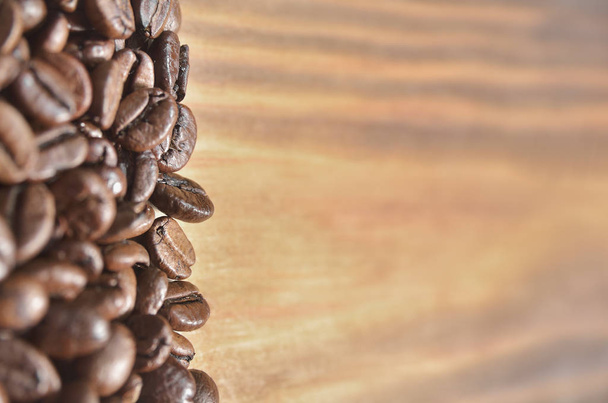 Beautiful fried coffee beans on a light wooden background, on the left. Background, wallpaper - Foto, Imagen