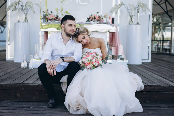 daytime portrait of bride and groom sitting on wooden deck  - Фото, изображение