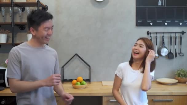 Beautiful happy asian couple are dancing in the kitchen at home. Young asian couple have romantic time while listening music at home. - Filmagem, Vídeo