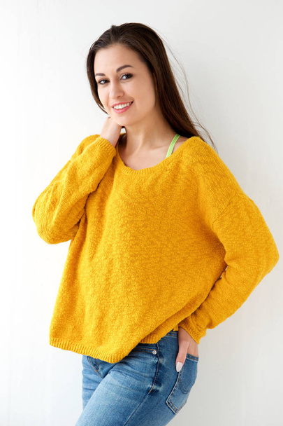 Portrait of attractive young woman smiling in yellow sweater against white wall - 写真・画像