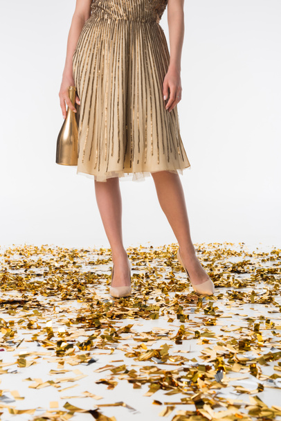 cropped image of woman standing on confetti in dress and holding golden bottle of champagne - Fotoğraf, Görsel