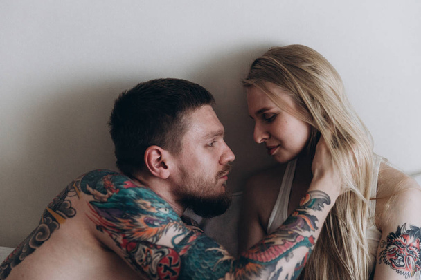 Чувственный татуированный мужчина обнимает блондинку в постели
 - Фото, изображение