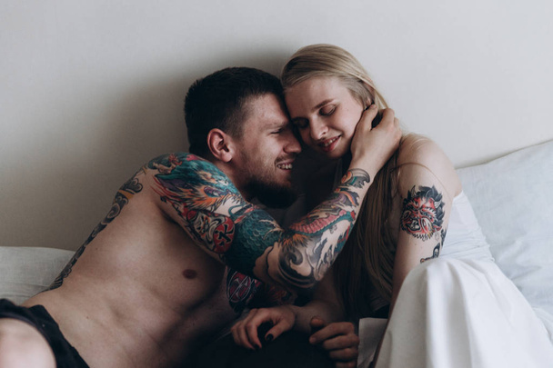 Sensual tattooed man embracing girl in bed - Фото, зображення