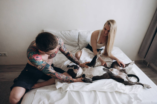 Young couple sitting on bed and fooling with dog - Foto, immagini