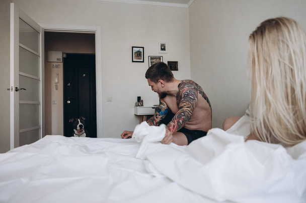 Side view of young couple on bed looking at dog in doorway - Foto, Bild