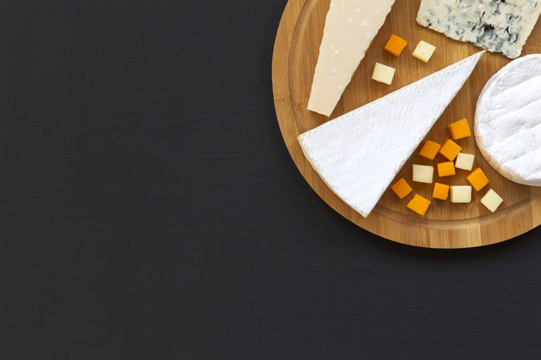 Various types of cheese on round wooden board, top view. Dark background. Space for text. Flat lay. From above. - Fotoğraf, Görsel