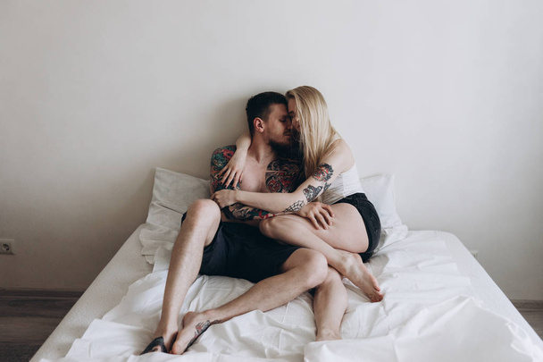 Young tattooed couple sensually embracing on bed at home - Foto, Imagen