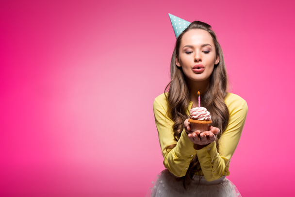 jolie femme avec chapeau de fête tenant cupcake et soufflant bougie isolée sur rose
 - Photo, image