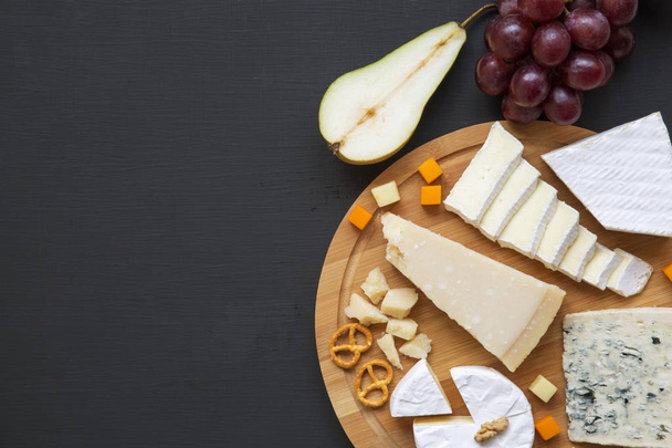 Tasting cheese with fruits, pretzels and walnuts on dark background, from above. Food for wine. Top view. Copy space. - Foto, afbeelding