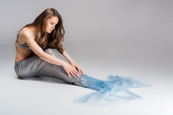 приваблива жінка з хвіст русалки сидить на підлозі і торкається ніг
 - Фото, зображення