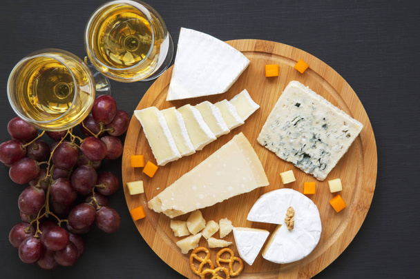 Verkostung von Käse mit Wein, Trauben, Brezeln und Walnüssen auf dunklem Hintergrund, von oben. Essen für Wein. Ansicht von oben.  - Foto, Bild
