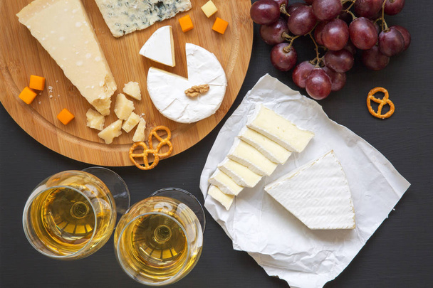 Cheese platter with wine, fruits, pretzels and walnuts on dark background, from above.Top view. Flat lay. - Photo, Image