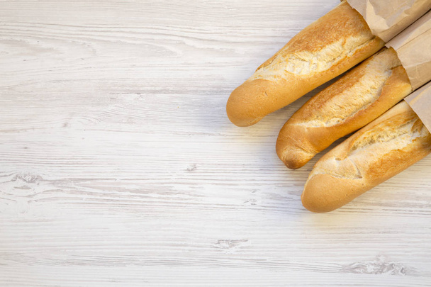 French baguettes in paper bags on white wooden table, top view. Copy space. - Photo, Image