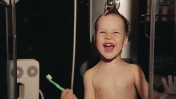 少し変な 2-3 歳の少年がシャワーと笑いで歯を磨く - 映像、動画