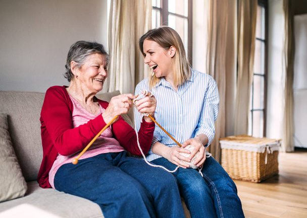 Elderly grandmother and adult granddaughter at home, knitting. - Foto, afbeelding