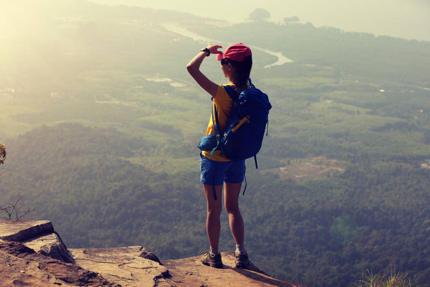 山のピークの崖の端に立っている成功した女性ハイカー - 写真・画像