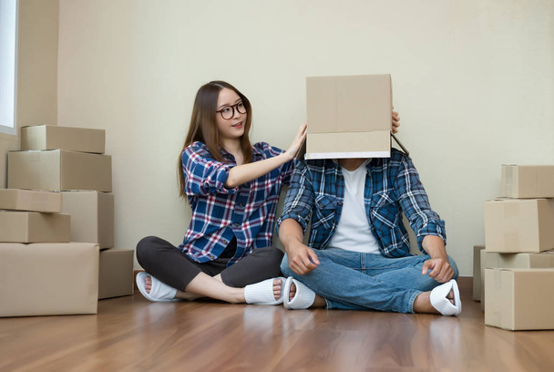 Joyeux couple avec des boîtes en carton sur la tête assis sur le sol après le déménagement
. - Photo, image