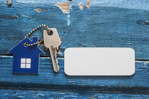 House key on a house shaped keychain resting on wooden background, concept for real estate - Photo, Image