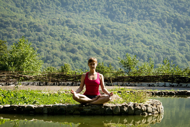 menina em shorts e t-shirt meditando na margem de um lago de montanha sentado à beira da água
 - Foto, Imagem